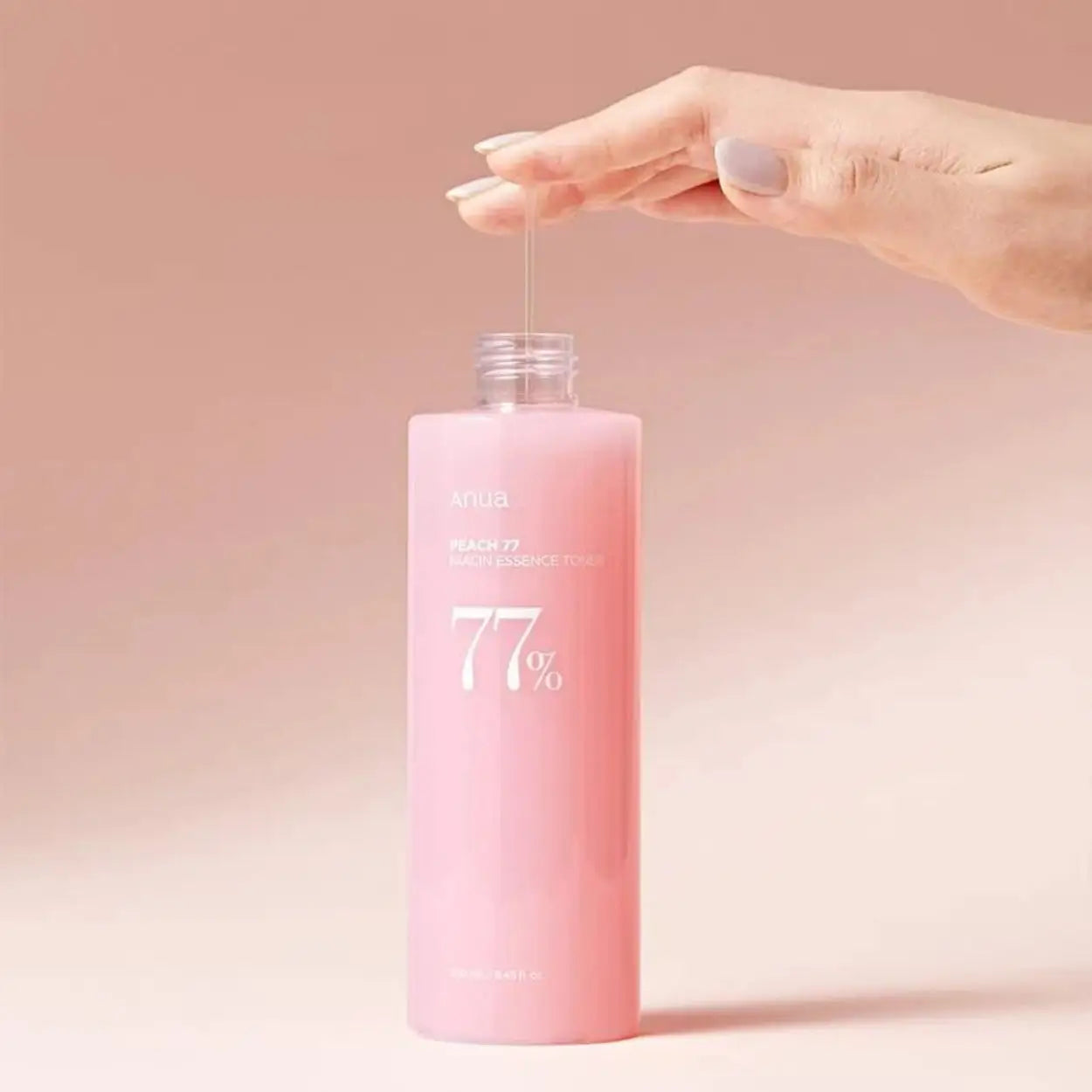 ANUA Peach 77% Niacin Essence Toner segurado por uma mão em fundo rosa – tónico essência com 77% de extrato de pêssego para uma pele mais luminosa e hidratada, cosmética coreana, skincare k-beauty Portugal