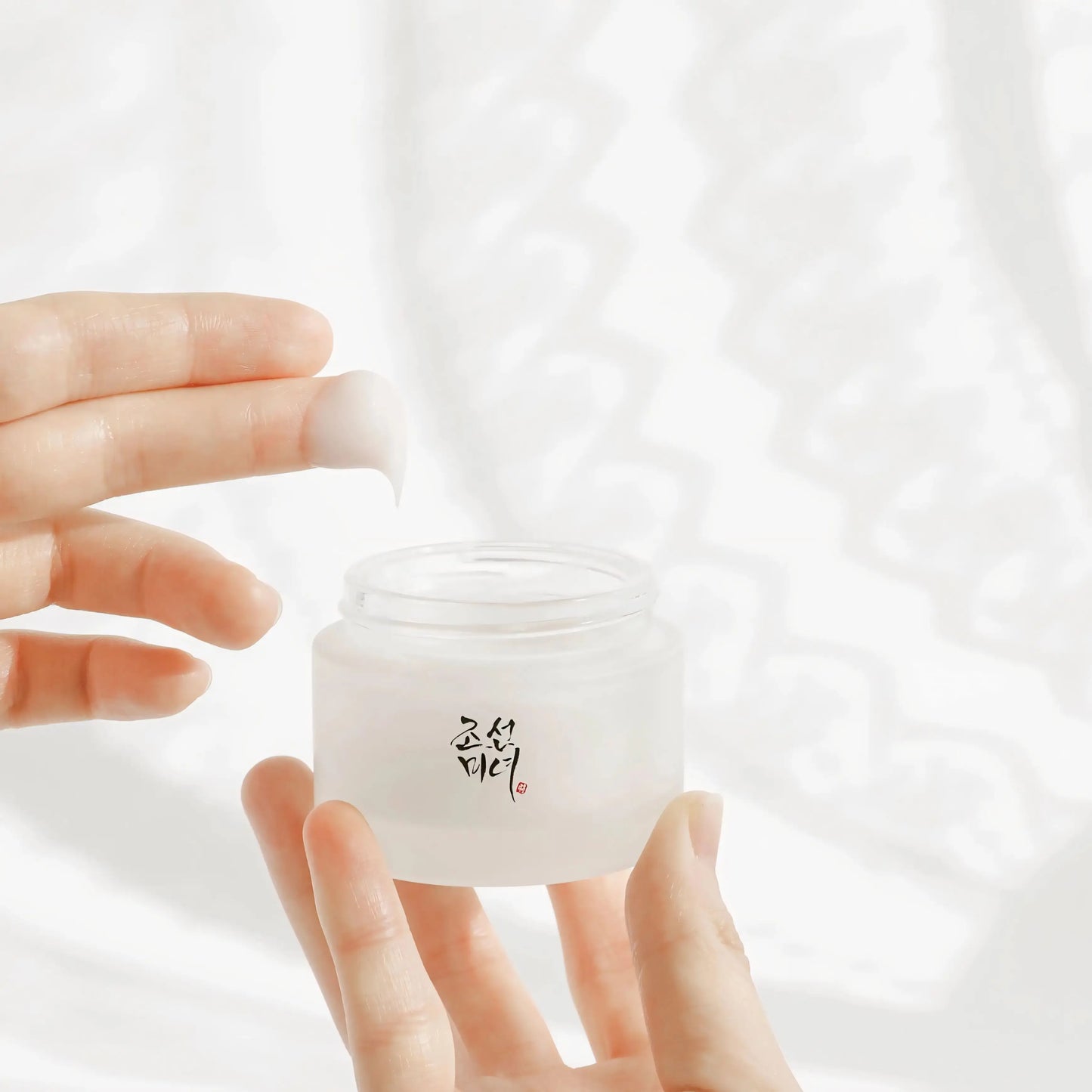 Frasco da Beauty of Joseon Dynasty Cream 50ml segurado na mão com tecido branco – creme facial coreano para hidratação intensa, pele luminosa e uniforme, cosmética coreana, skincare k-beauty Portugal