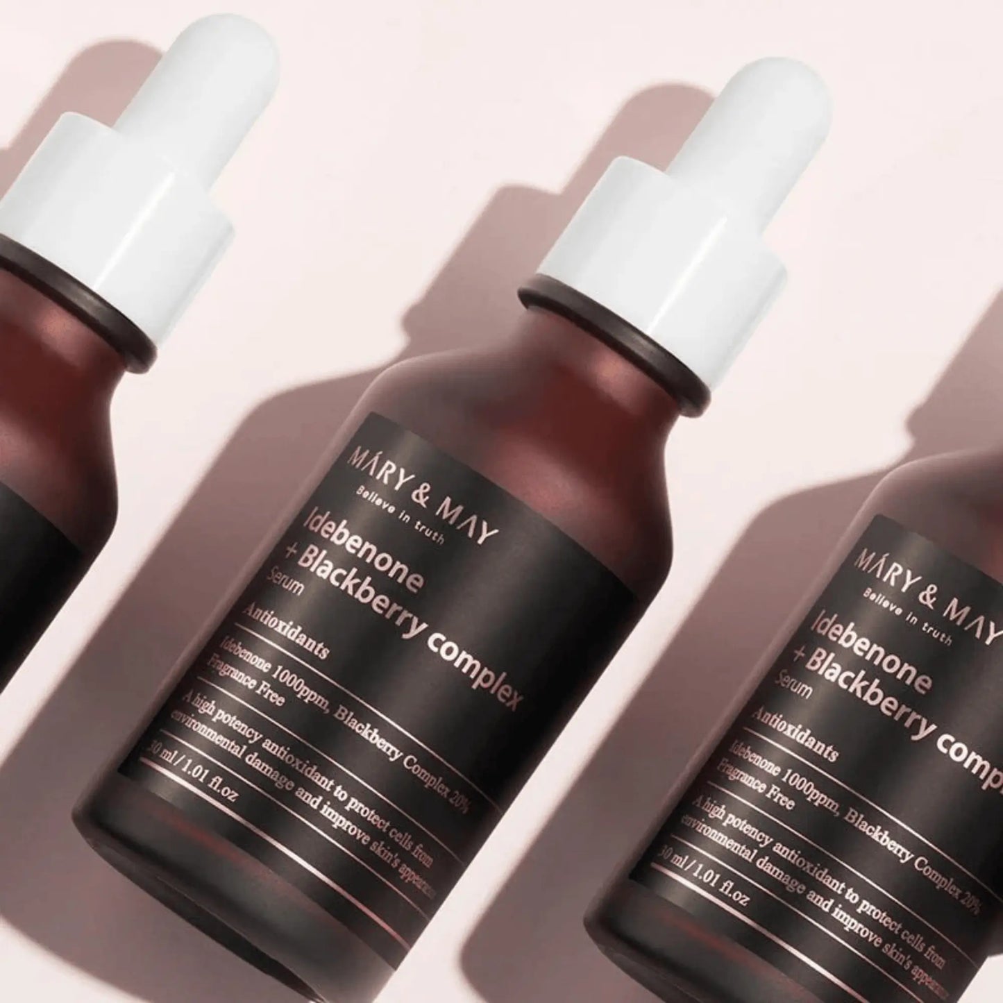 Mary & May Idebenone + Blackberry Complex Serum 30ml, sérum coreano com idebenona e antioxidantes de amora-preta, suaviza rugas e reforça elasticidade, close-up de dois frascos deitados lado a lado sobre fundo rosa claro, cosmética coreana skincare k-beauty Portugal.
