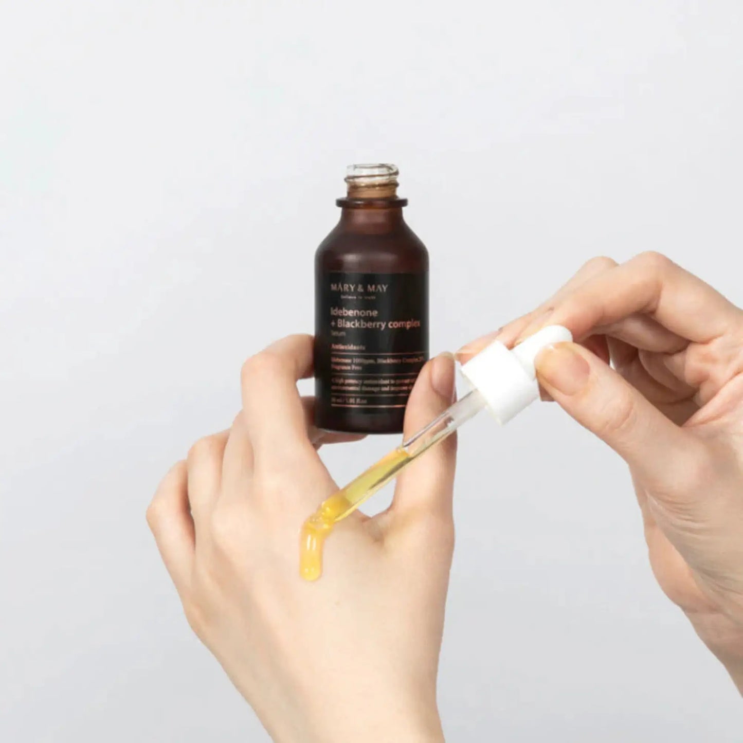 Mary & May Idebenone + Blackberry Complex Serum 30ml, sérum facial coreano antioxidante que ilumina a pele e combate sinais de idade, mão feminina a segurar frasco aberto com conta-gotas, fundo branco, cosmética coreana skincare k-beauty Portugal.