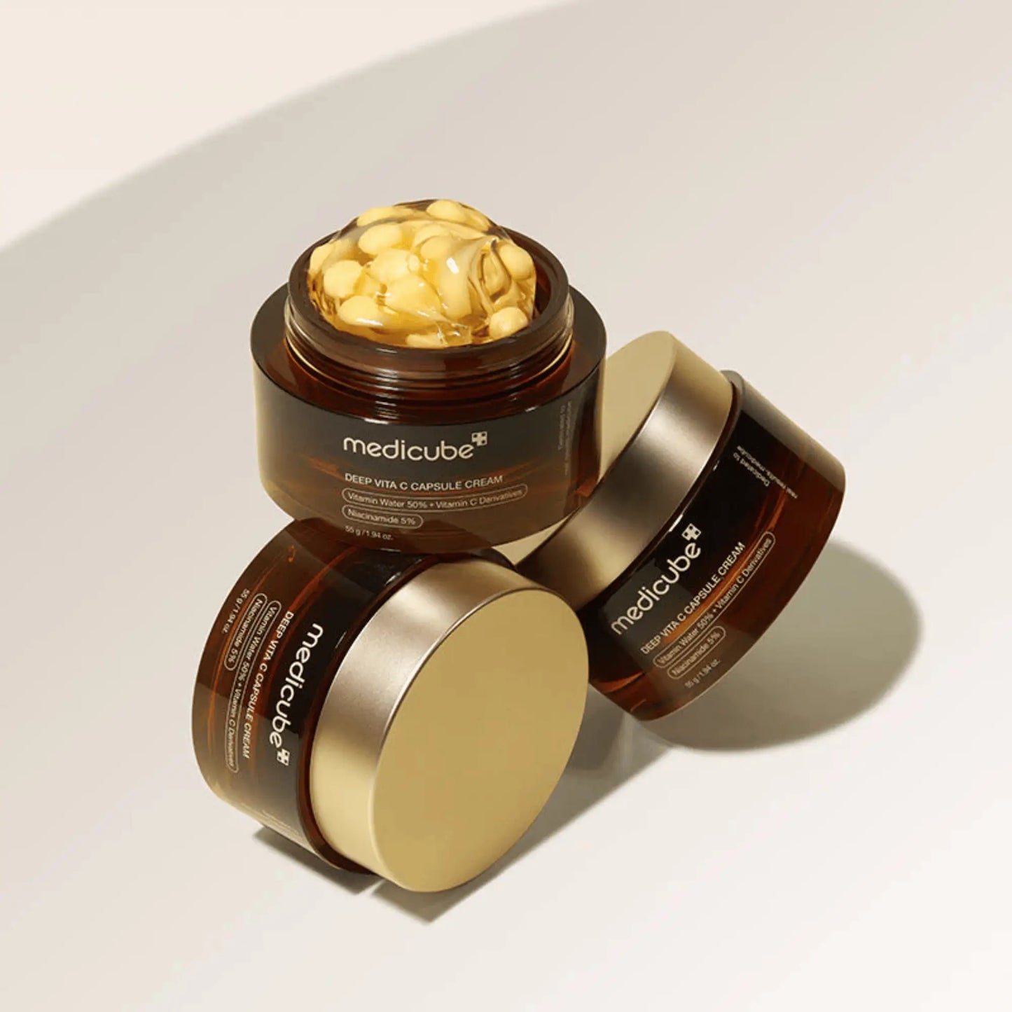 Medicube Deep Vita C Capsule Cream 55g, creme facial coreano iluminador com vitamina C encapsulada, melhora firmeza e uniformiza o tom da pele, dois frascos empilhados com cápsulas douradas visíveis, fundo dourado, cosmética coreana skincare k-beauty Portugal.