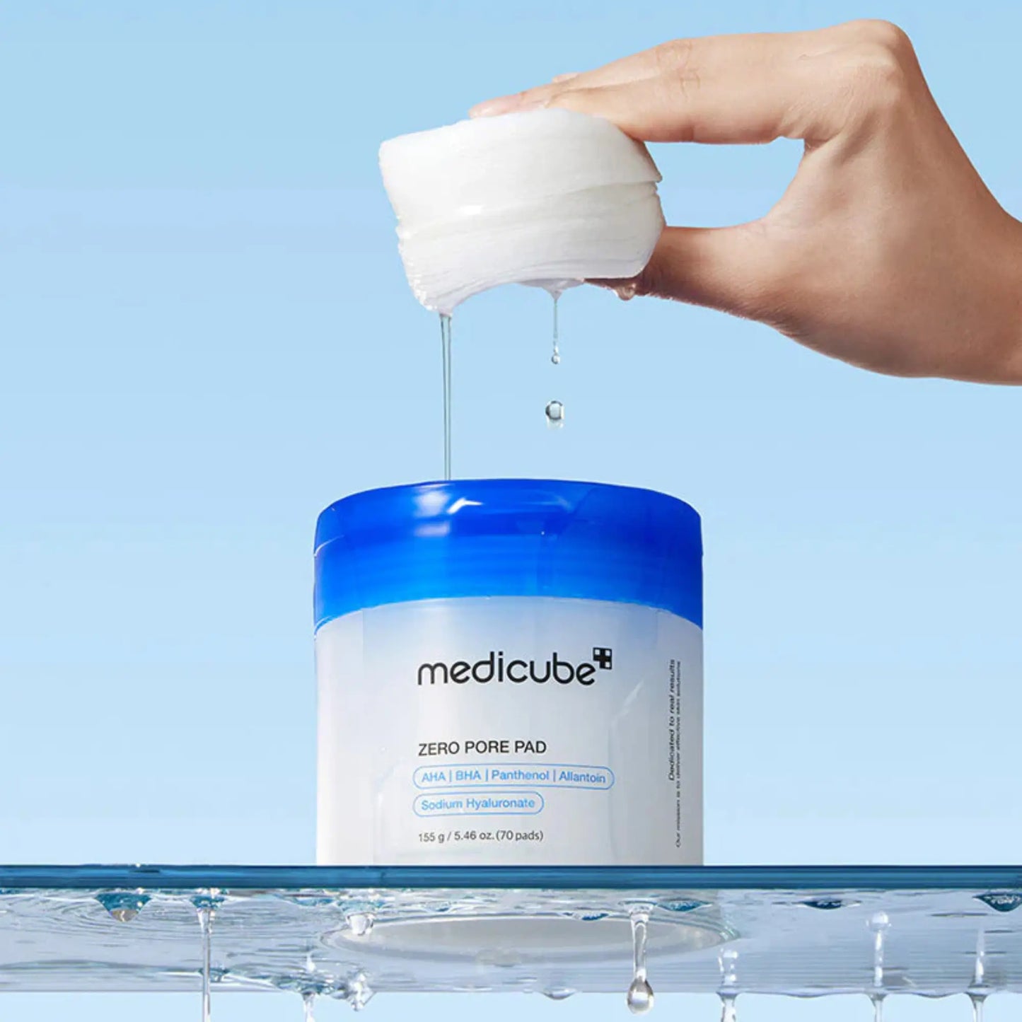 Medicube Zero Pore Pad 2.0 (70pcs), exfoliante facial coreano com discos embebidos em solução de AHA, BHA e PHA para limpar poros e suavizar imperfeições, mão a retirar disco com pinça azul de frasco sobre superfície branca, cosmética coreana skincare k-beauty Portugal.