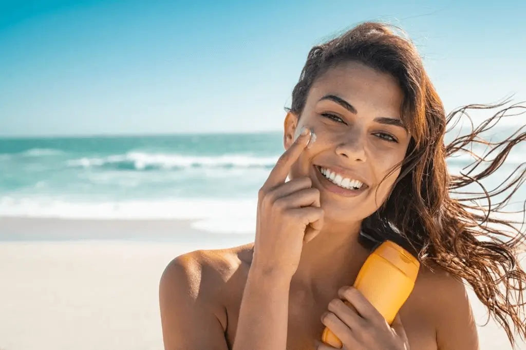 Mulher a aplicar protetor solar com sorriso na praia — proteção solar diária como último passo da rotina de skincare coreano para rosto. Essencial para prevenir manchas, envelhecimento precoce e proteger dos raios UV. Cosmética coreana com SPF – skincare k-beauty Portugal.