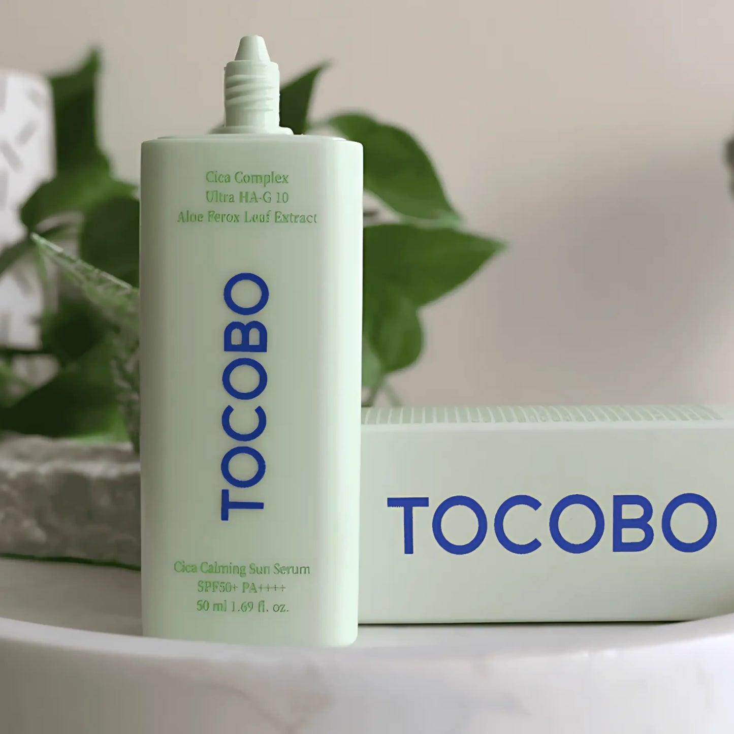 TOCOBO Cica Calming Sun Serum – embalagem minimalista com design verde e branco ao lado da caixa, refletindo a estética clean da cosmética coreana e o foco em ingredientes calmantes