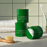 Três embalagens de Dr. Althea Pure Grinding Cleansing Balm numa bancada de casa de banho, uma delas aberta.