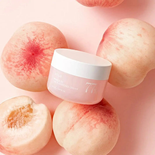 ANUA Peach 77% Niacin Enriched Cream rodeado de pêssegos sobre fundo rosa – creme coreano nutritivo com niacinamida e 77% de pêssego para iluminar e suavizar a pele, cosmética coreana, skincare k-beauty Portugal