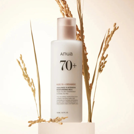 Anua Rice 70 Intensive Moisturizing Milk 150ml, loção facial coreana hidratante com 70% de extrato de arroz para hidratação profunda, luminosidade e reforço da barreira cutânea, frasco em pé com espigas de arroz ao fundo sobre fundo bege suave, cosmética coreana skincare k-beauty Portugal.