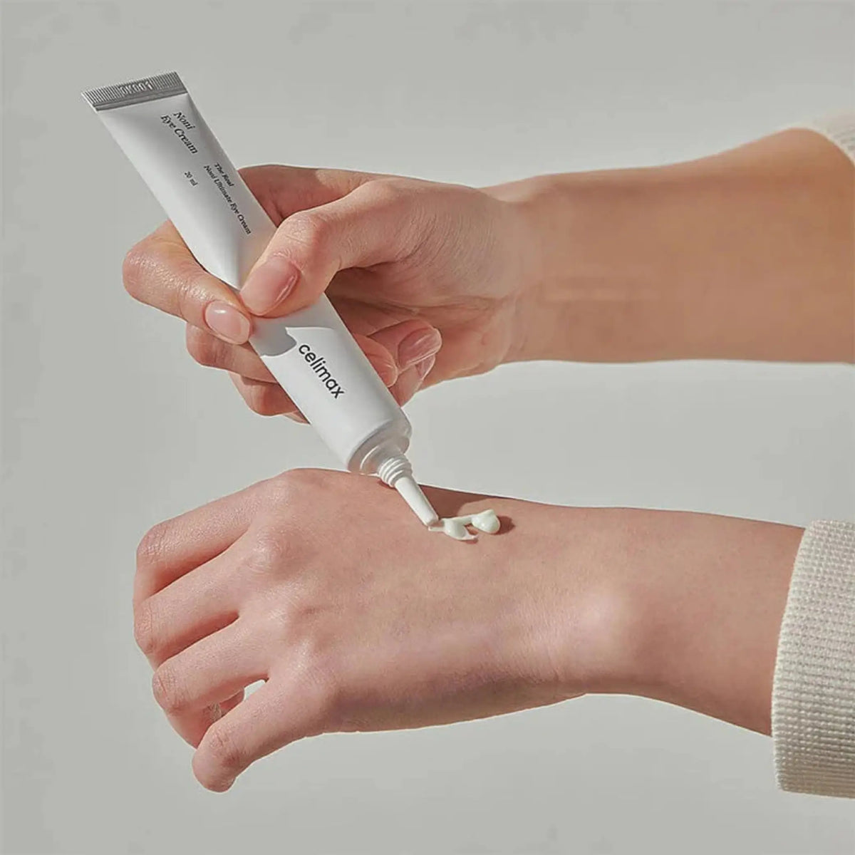 The Real Noni Ultimate Eye Cream da Celimax em tubo na mão com creme aplicado na pele
