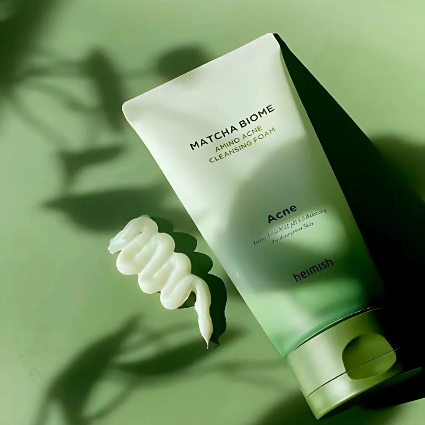 Heimish Matcha Biome Amino Acne Cleansing Foam 150g, espuma de limpeza facial coreana com chá verde matcha antioxidante e aminoácidos calmantes, ajuda a purificar poros e acalmar irritações, frasco em pé com sombra de folhas verdes projetada sobre fundo verde claro, cosmética coreana skincare k-beauty Portugal.