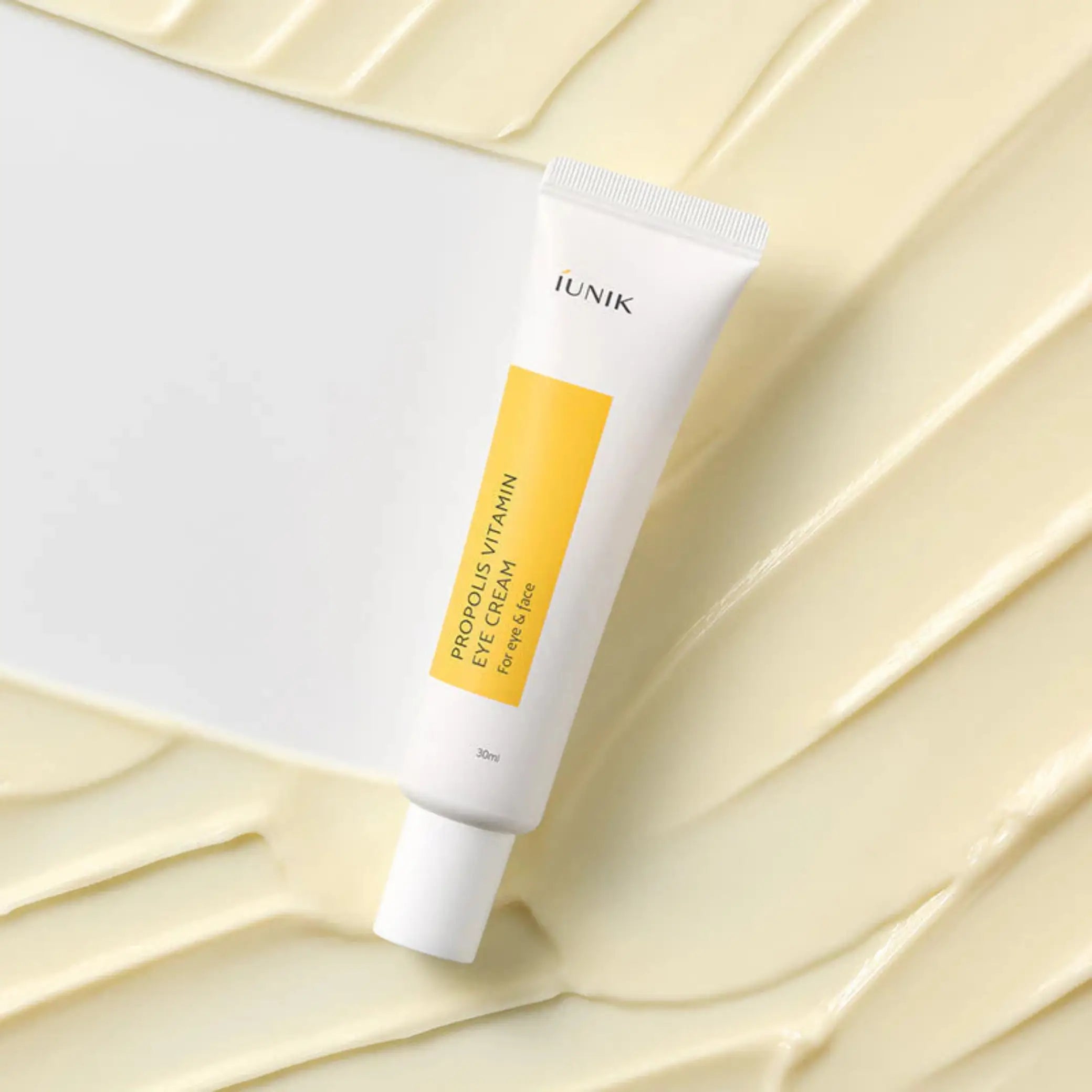 Propolis Vitamin Eye Cream da iUNIK tubo sobre textura de creme em fundo bege
