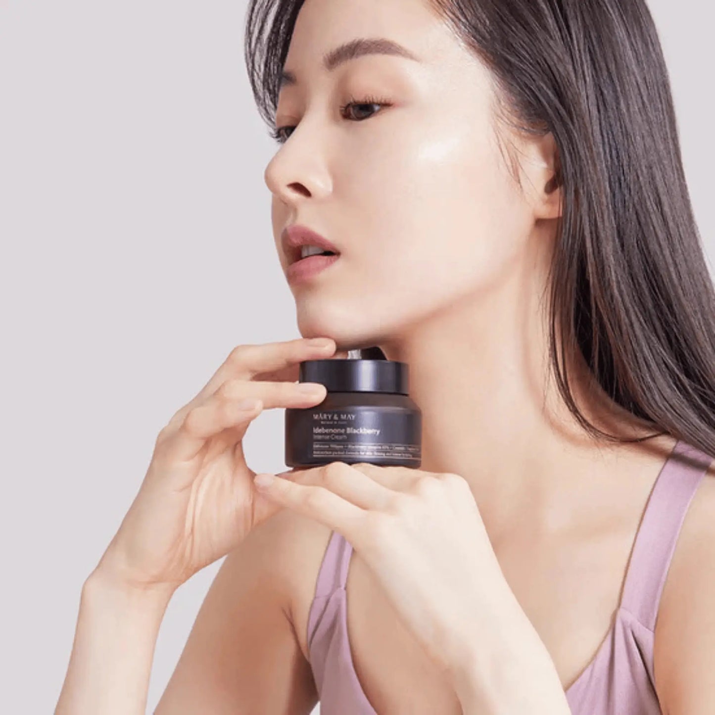 Mary & May Idebenone + Blackberry Complex Intensive Total Care Cream 70g, creme coreano antioxidante que reduz rugas, ilumina e dá firmeza, modelo feminina a segurar o frasco junto ao rosto, fundo claro, cosmética coreana skincare k-beauty Portugal.