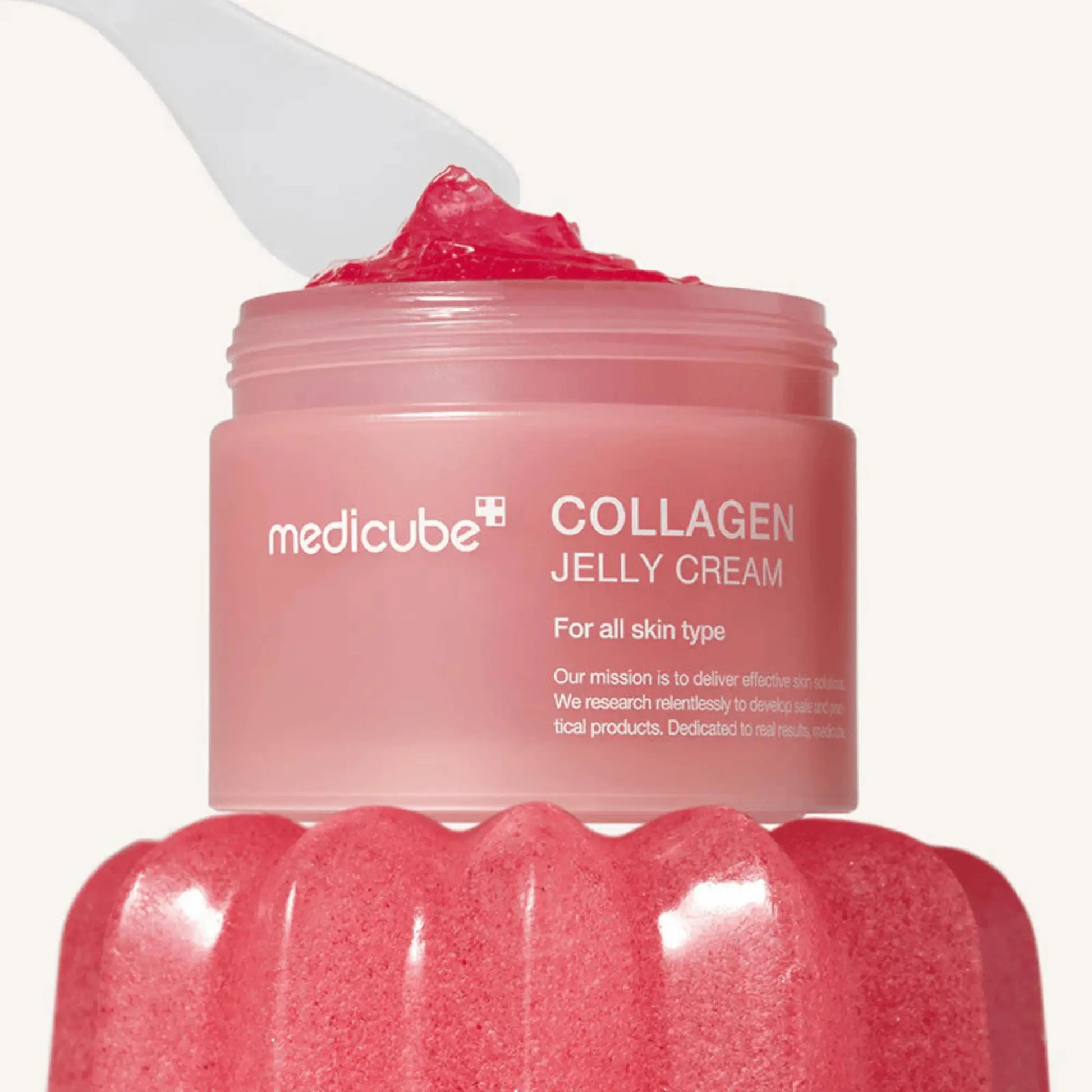 Medicube Collagen Jelly Cream 110ml, creme coreano facial anti-envelhecimento com colagénio e textura jelly para hidratar, firmar e dar luminosidade, close-up do frasco aberto com espátula a levantar o creme rosa, cosmética coreana skincare k-beauty Portugal.