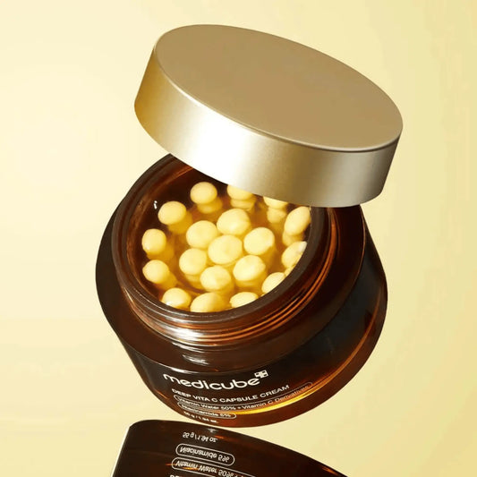 Medicube Deep Vita C Capsule Cream 55g, creme facial coreano iluminador com vitamina C encapsulada e antioxidantes, ajuda a reduzir manchas, uniformizar o tom e dar luminosidade, frasco aberto com cápsulas douradas visíveis sobre fundo dourado, cosmética coreana skincare k-beauty Portugal.