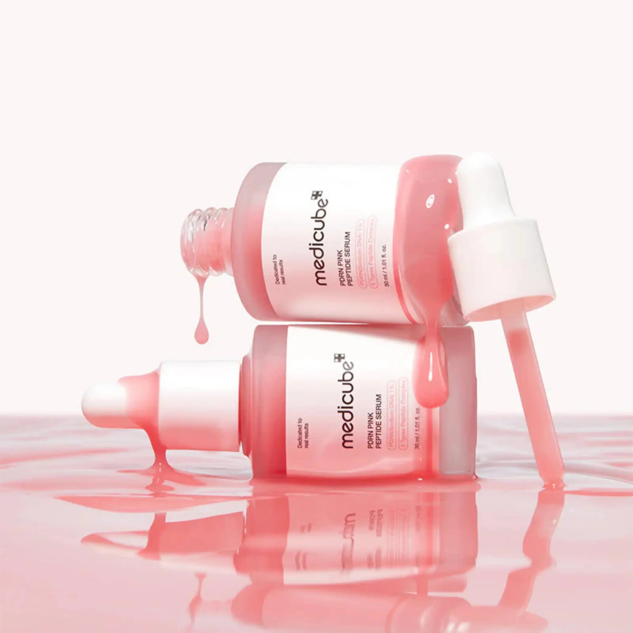 PDRN Pink Peptide Face Serum da medicube dois frascos com sérum a escorrer em fundo rosa