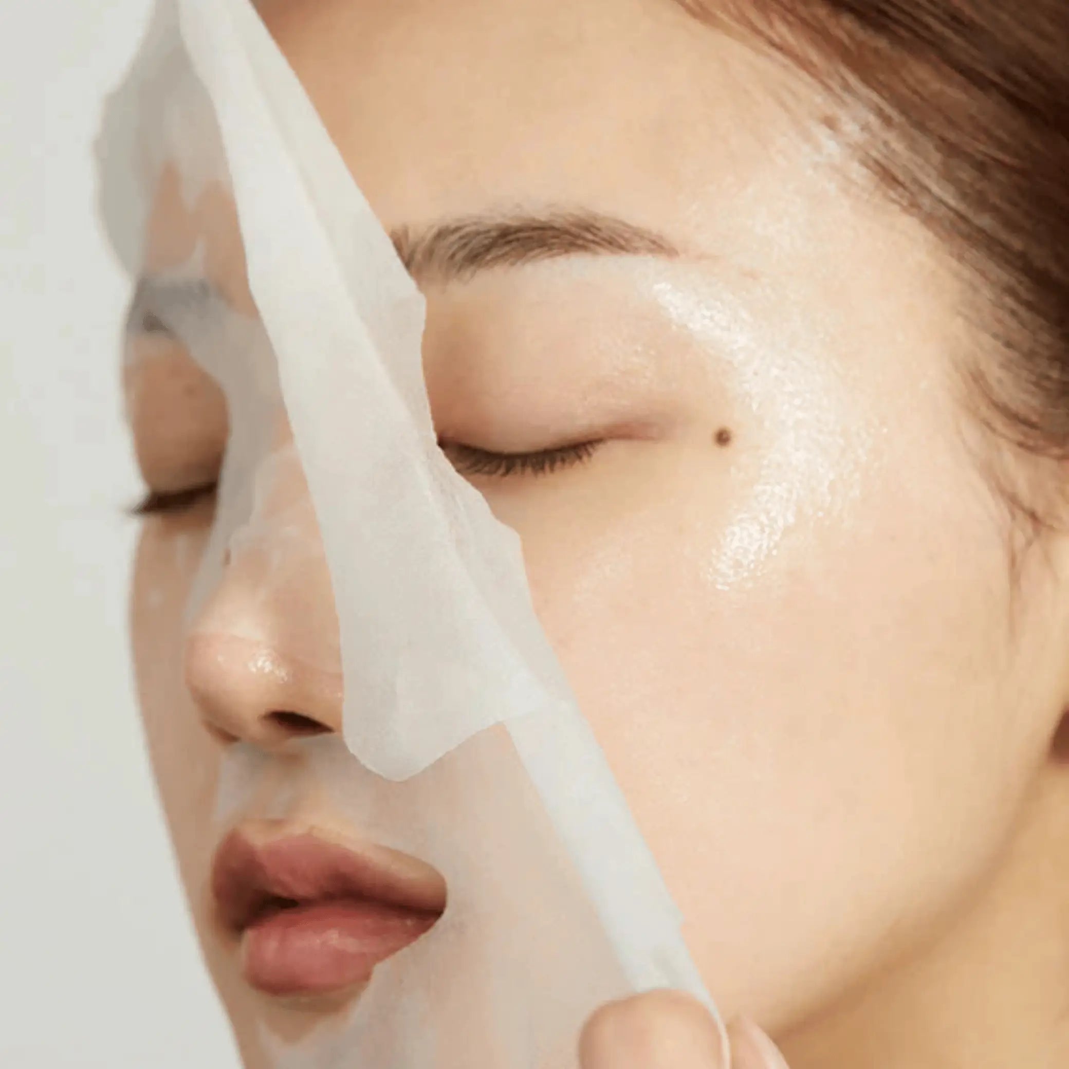Super Cica Calming Mask da Medicube modelo a retirar sheet mask do rosto em close-up