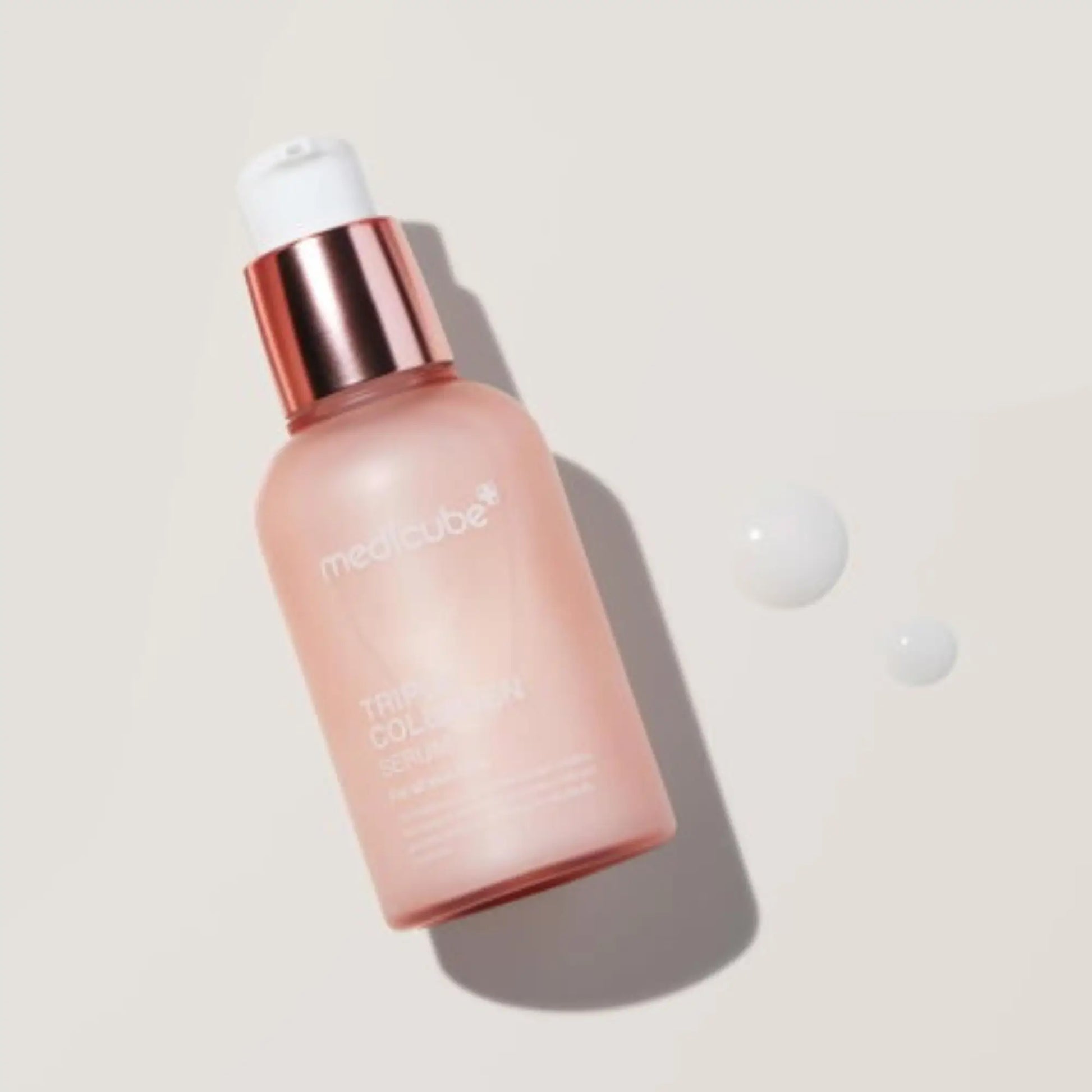 Medicube Triple Collagen Cream 4.0 50ml, creme facial coreano com colagénio triplo e péptidos que suavizam rugas e reforçam firmeza, frasco inclinado sobre fundo bege claro com duas gotas de creme ao lado, cosmética coreana skincare k-beauty Portugal.