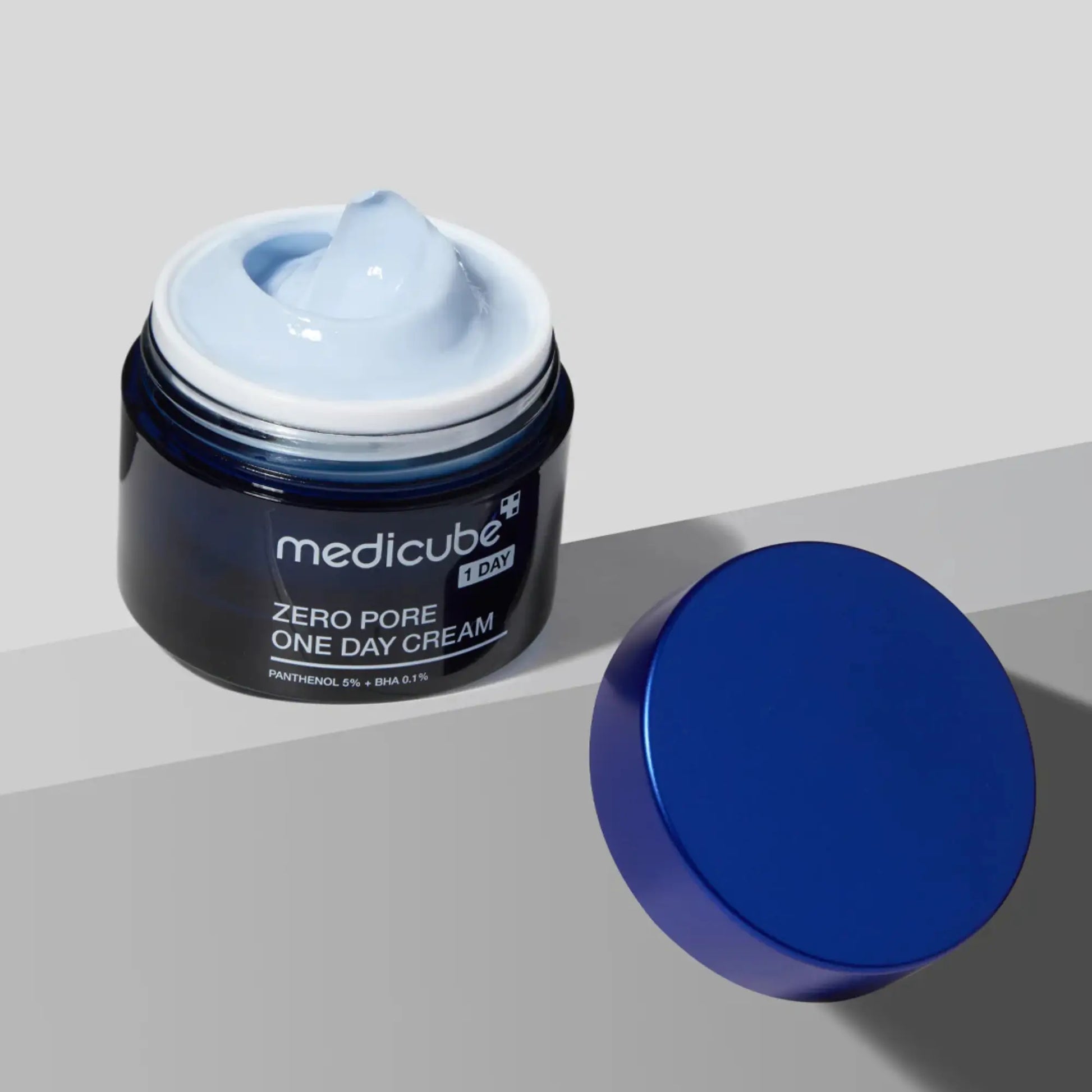Medicube Zero Pore One Day Cream 50ml, creme facial coreano para hidratação, firmeza e redução de poros, frasco aberto com creme visível e tampa azul ao lado sobre superfície cinzenta, cosmética coreana skincare k-beauty Portugal.