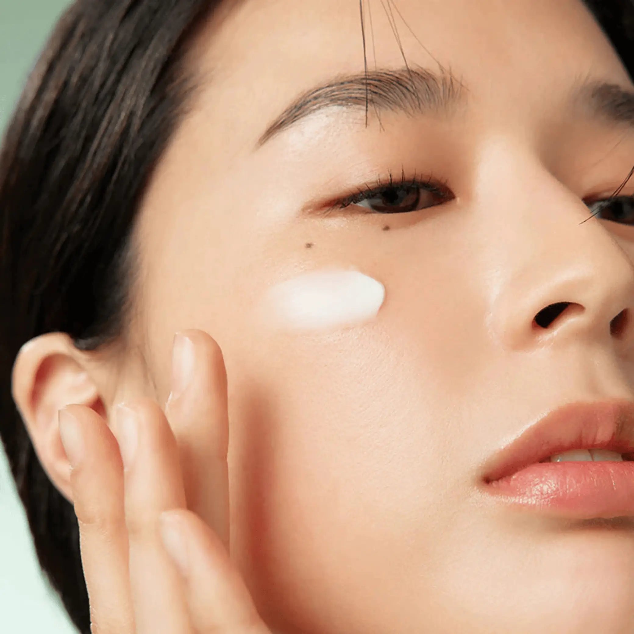 Wonder Releaf Centella Eye Cream Unscented da Purito Seoul creme na bochecha com mão a espalhar