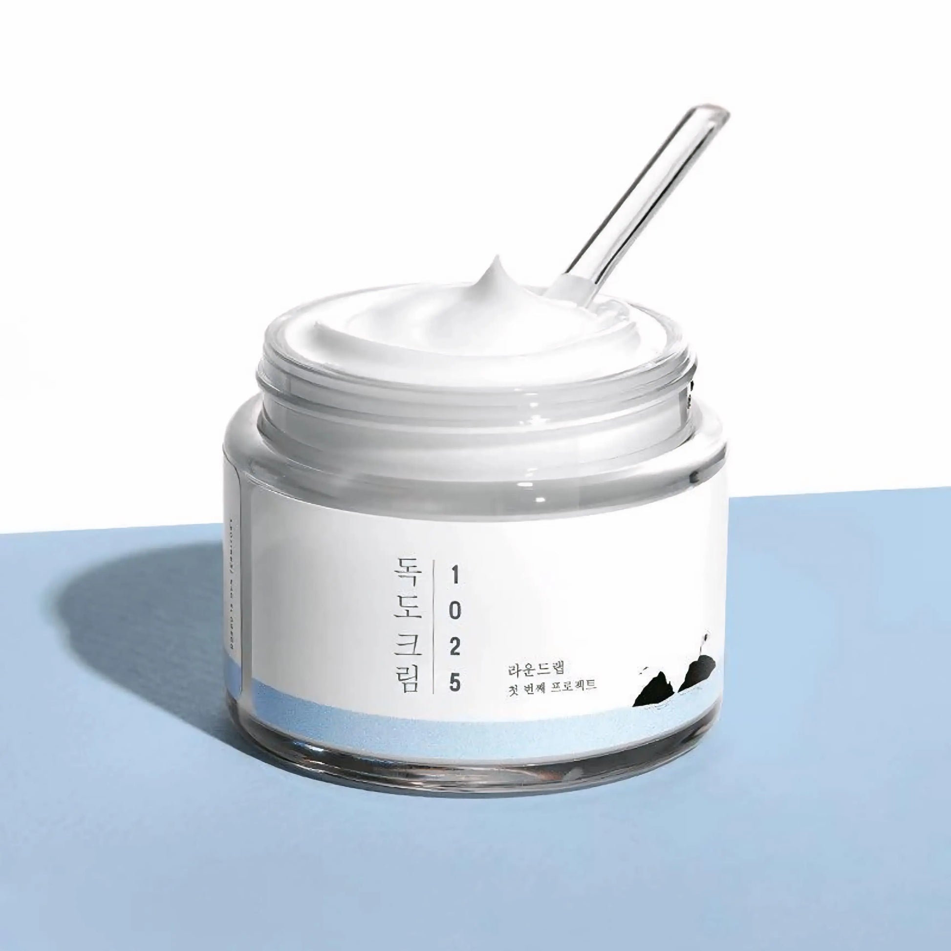 Round Lab 1025 Dokdo Cream — pote aberto com espátula visível, mostrando a textura rica e cremosa do creme hidratante. Cosmética coreana e skincare k-beauty Portugal.