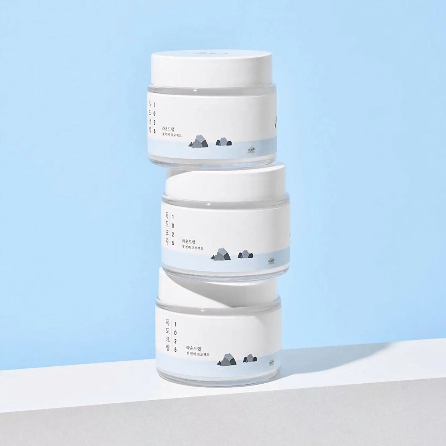 Round Lab 1025 Dokdo Cream — três embalagens empilhadas num fundo azul, representando reposição e uso contínuo para hidratação profunda. Cosmética coreana e skincare k-beauty Portugal.