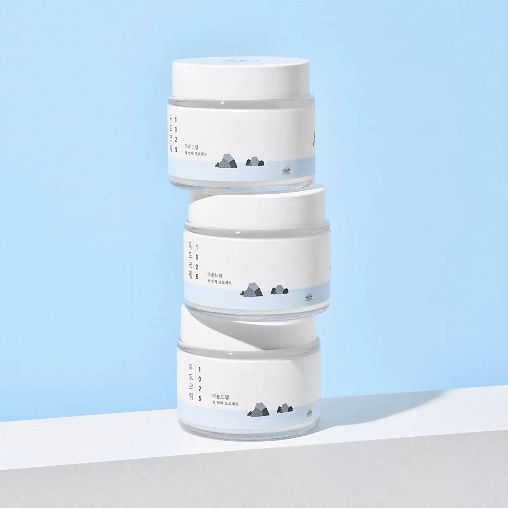 Round Lab 1025 Dokdo Cream — três embalagens empilhadas num fundo azul, representando reposição e uso contínuo para hidratação profunda. Cosmética coreana e skincare k-beauty Portugal.