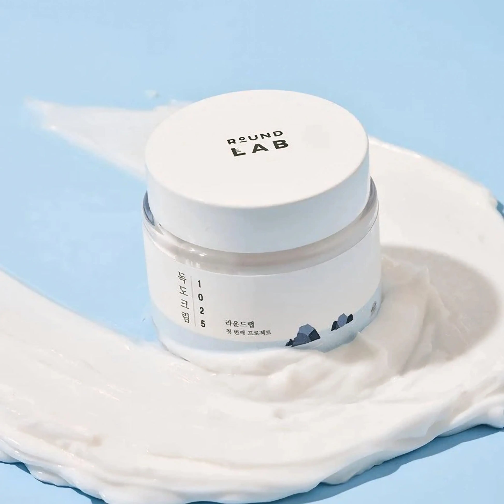Round Lab 1025 Dokdo Cream — embalagem inclinada sobre o próprio creme derramado, destacando a textura suave e nutritiva. Cosmética coreana e skincare k-beauty Portugal.