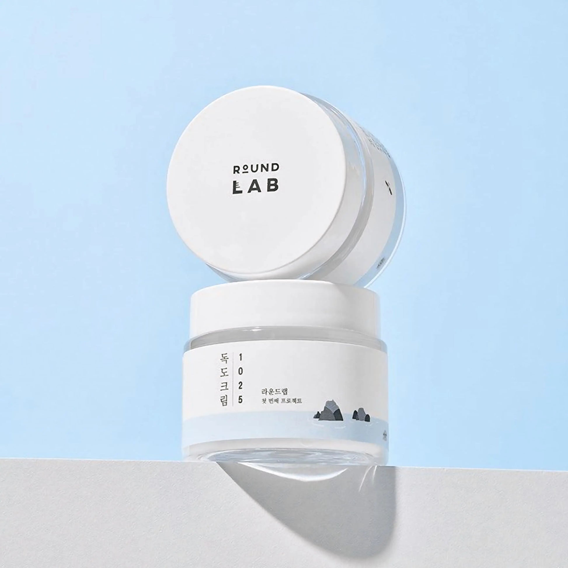 Round Lab 1025 Dokdo Cream — imagem do pote visto de cima, em fundo azul claro, transmitindo leveza e frescura. Cosmética coreana e skincare k-beauty Portugal.