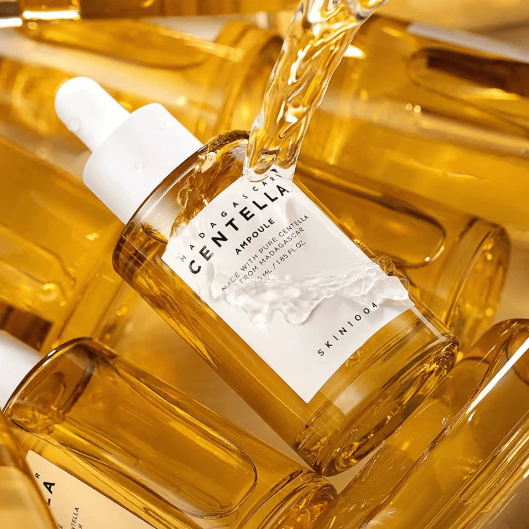 Madagascar Centella Ampoule da Skin1004 em frasco âmbar com líquido dourado a verter sobre a embalagem