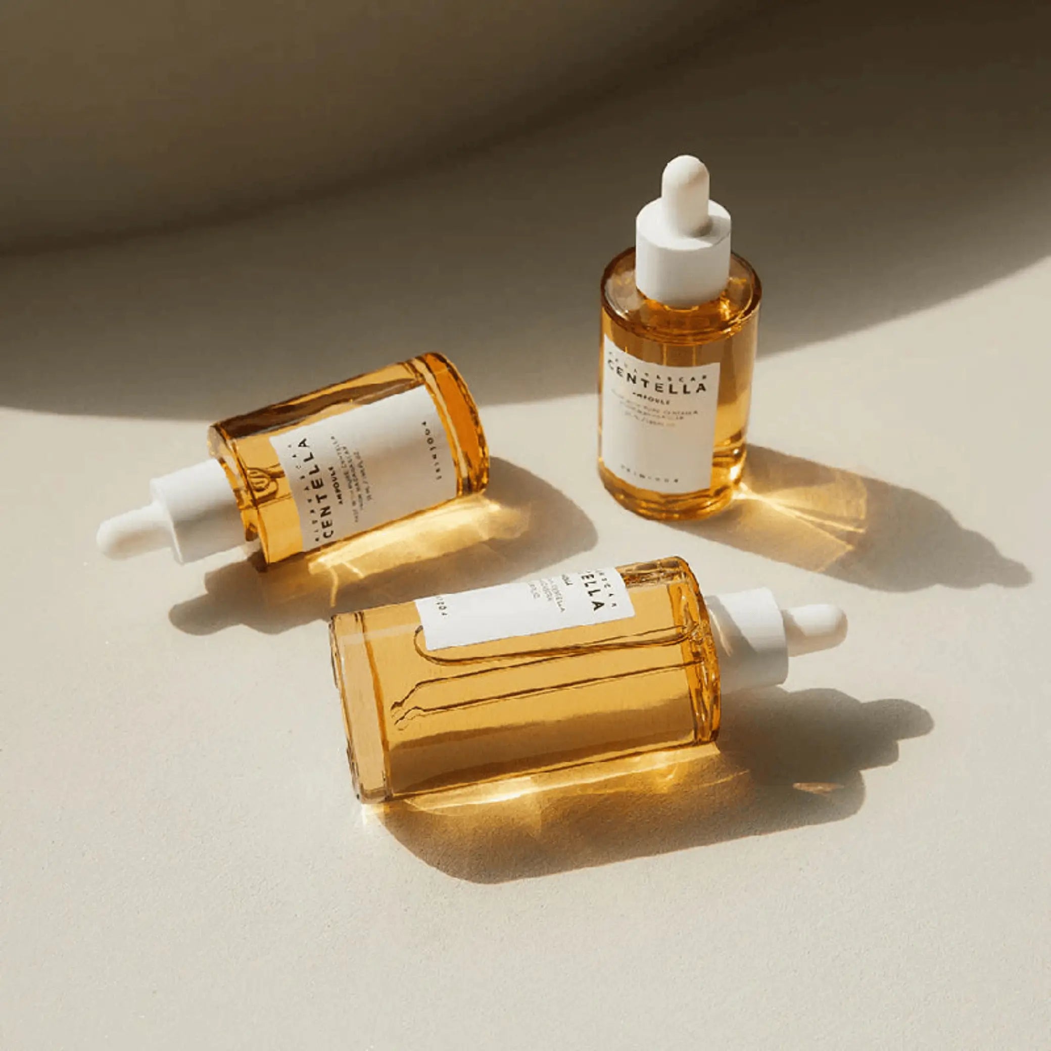 Madagascar Centella Ampoule da Skin1004 em três frascos âmbar dispostos sobre superfície bege com sombras naturais
