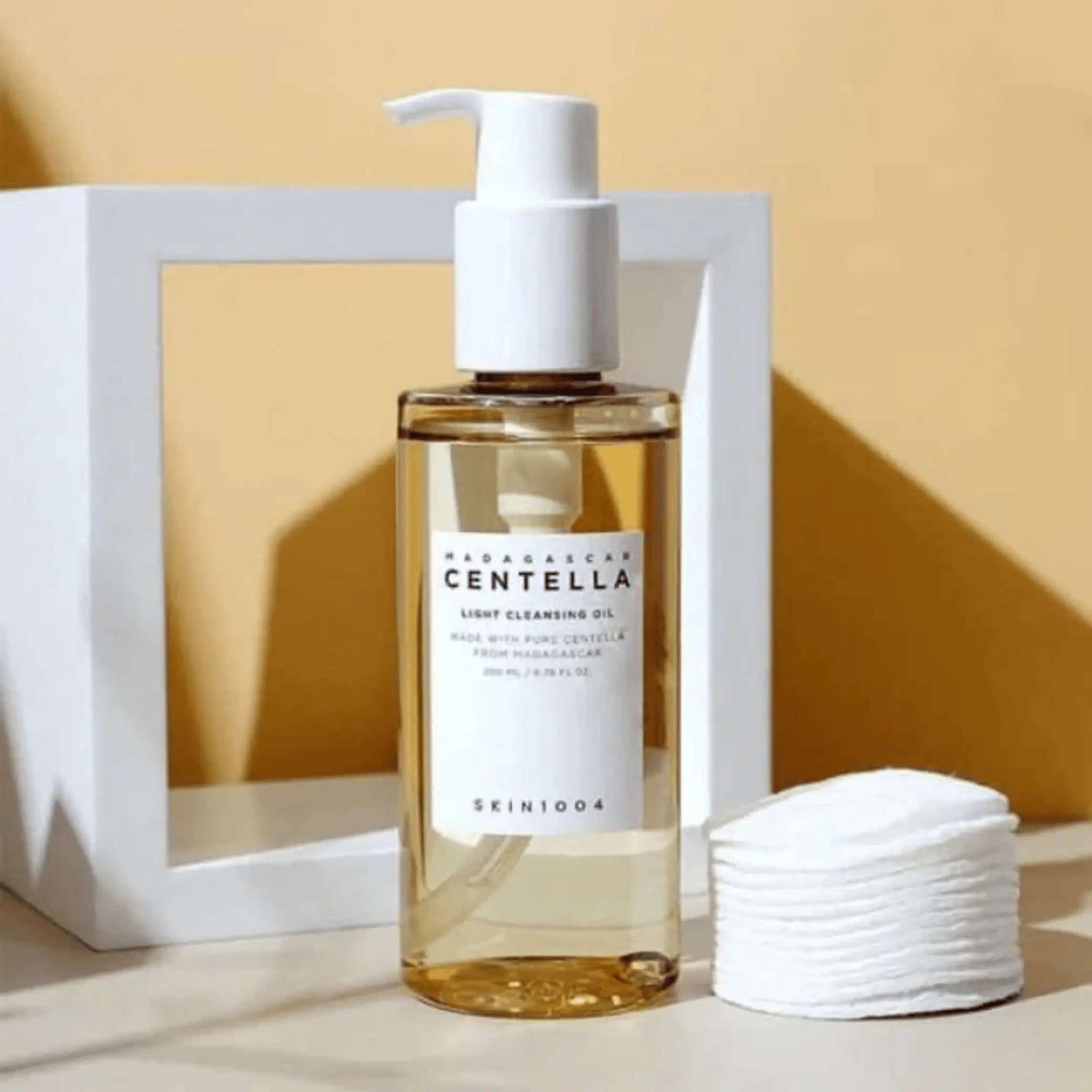 Madagascar Centella Light Cleansing Oil da Skin1004 em frasco com bomba ao lado de discos de algodão empilhados