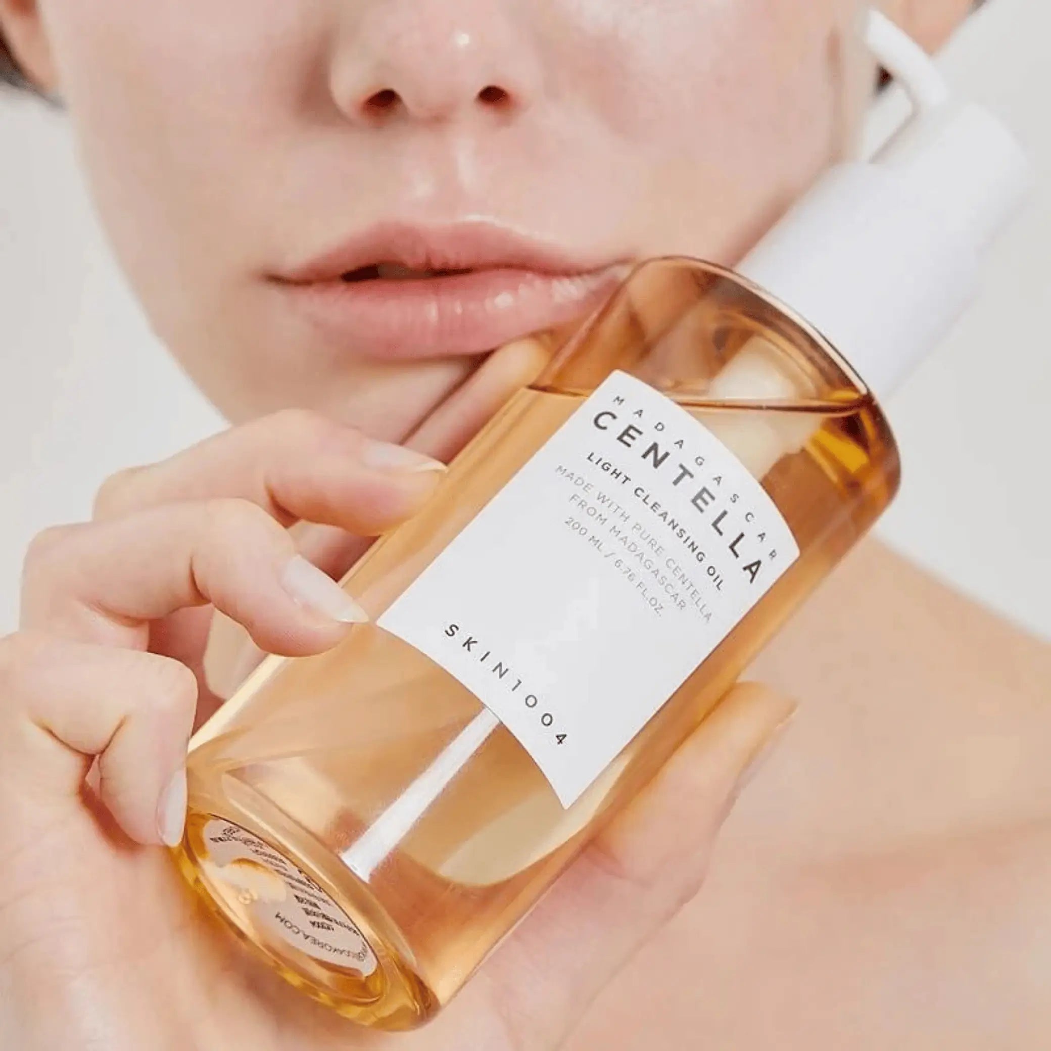 Madagascar Centella Light Cleansing Oil da Skin1004 modelo segura frasco âmbar junto ao rosto em close-up
