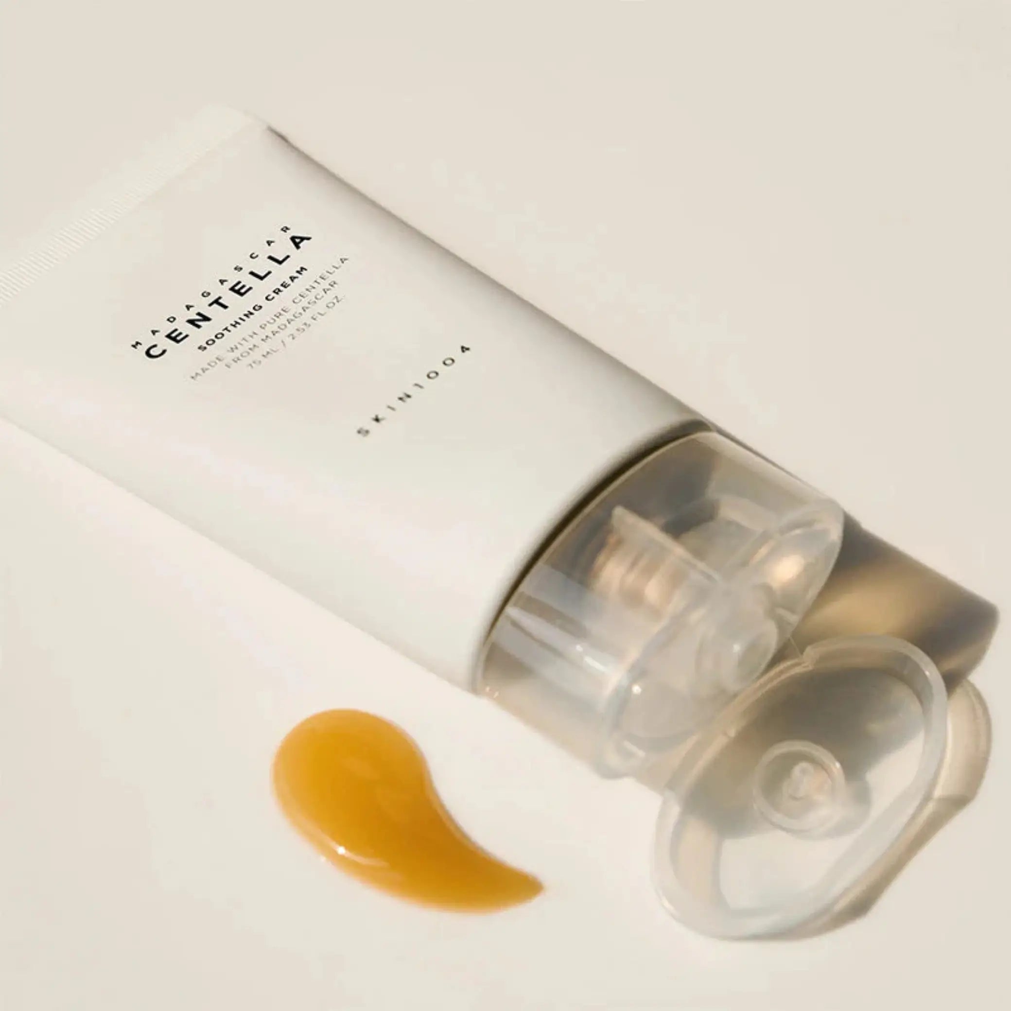 Madagascar Centella Soothing Cream da Skin1004 em bisnaga deitada com swipe de textura dourada ao lado