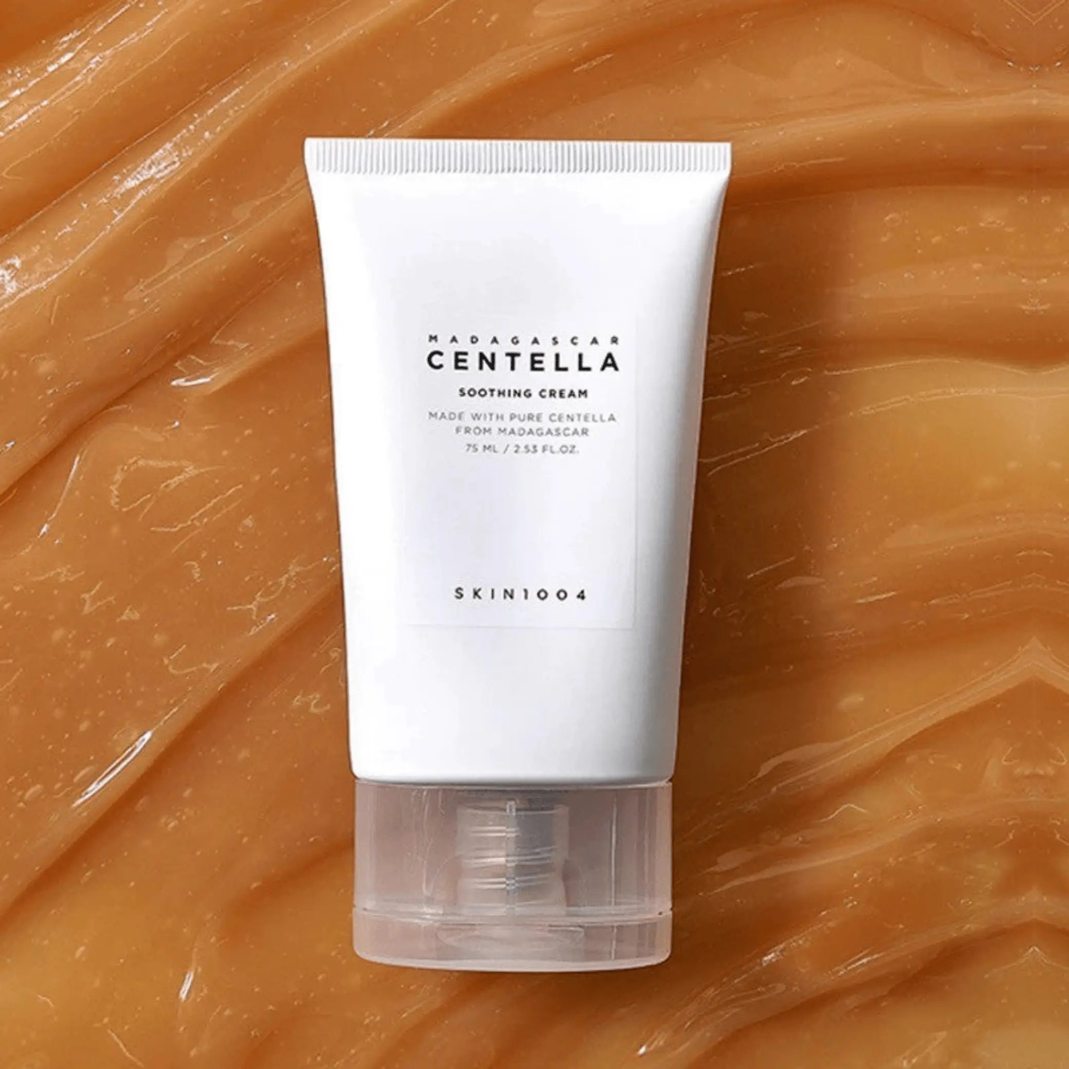 Madagascar Centella Soothing Cream da Skin1004 em bisnaga branca sobre fundo de textura dourada em swirl